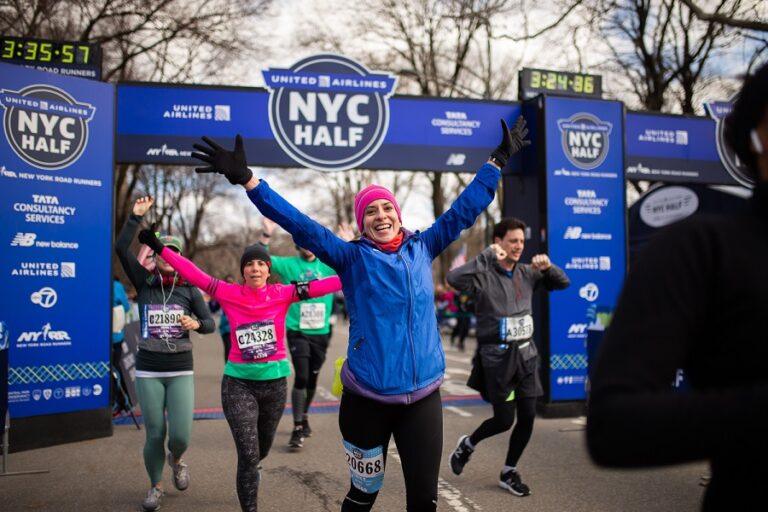 Coureuses franchissant joyeusement la ligne d'arrivée du NYC Half avec les bras levés en signe de victoire.