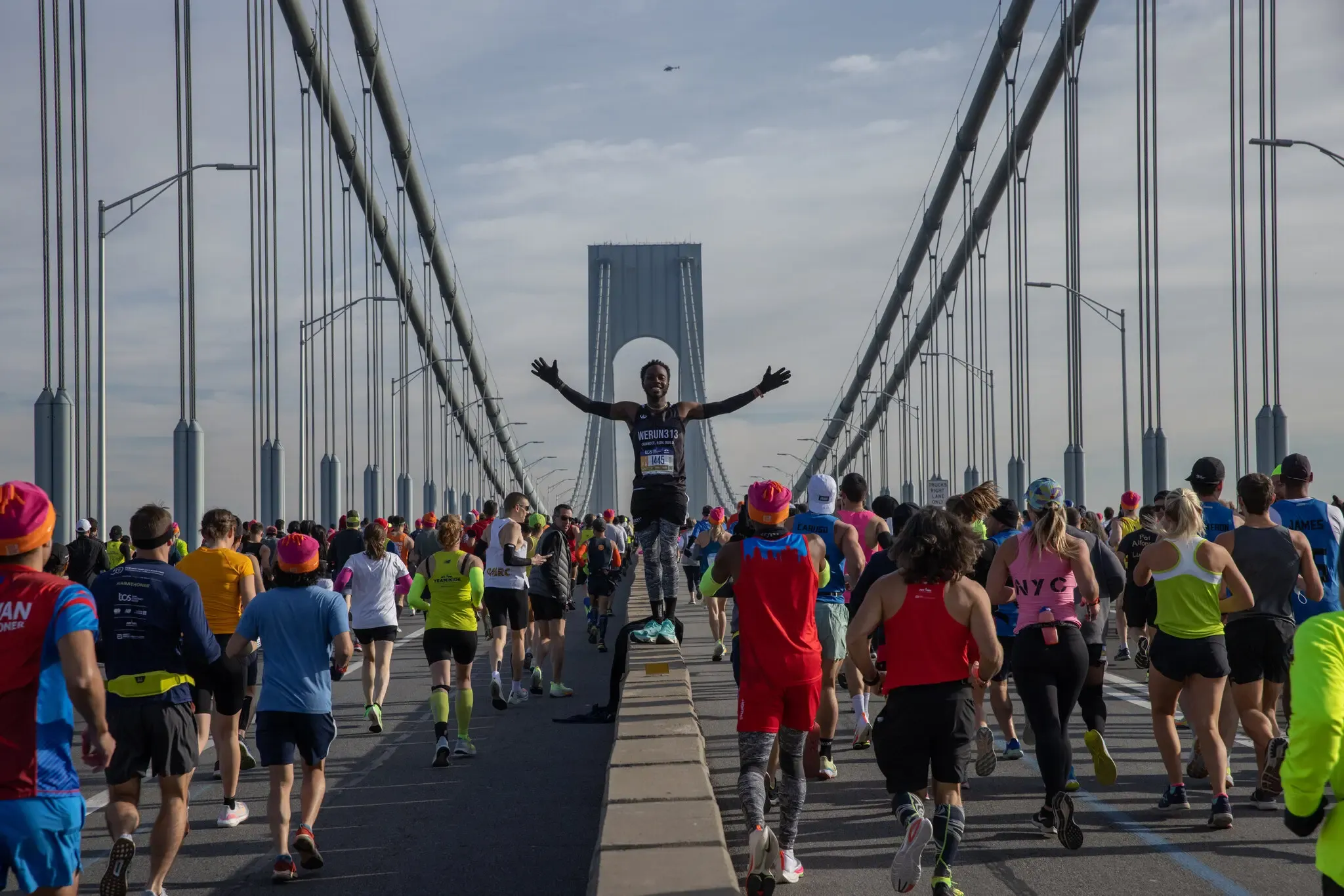 Coureur célébrant sur le Verrazano-Narrows Bridge avec les bras levés, entouré d'autres participants à la course.