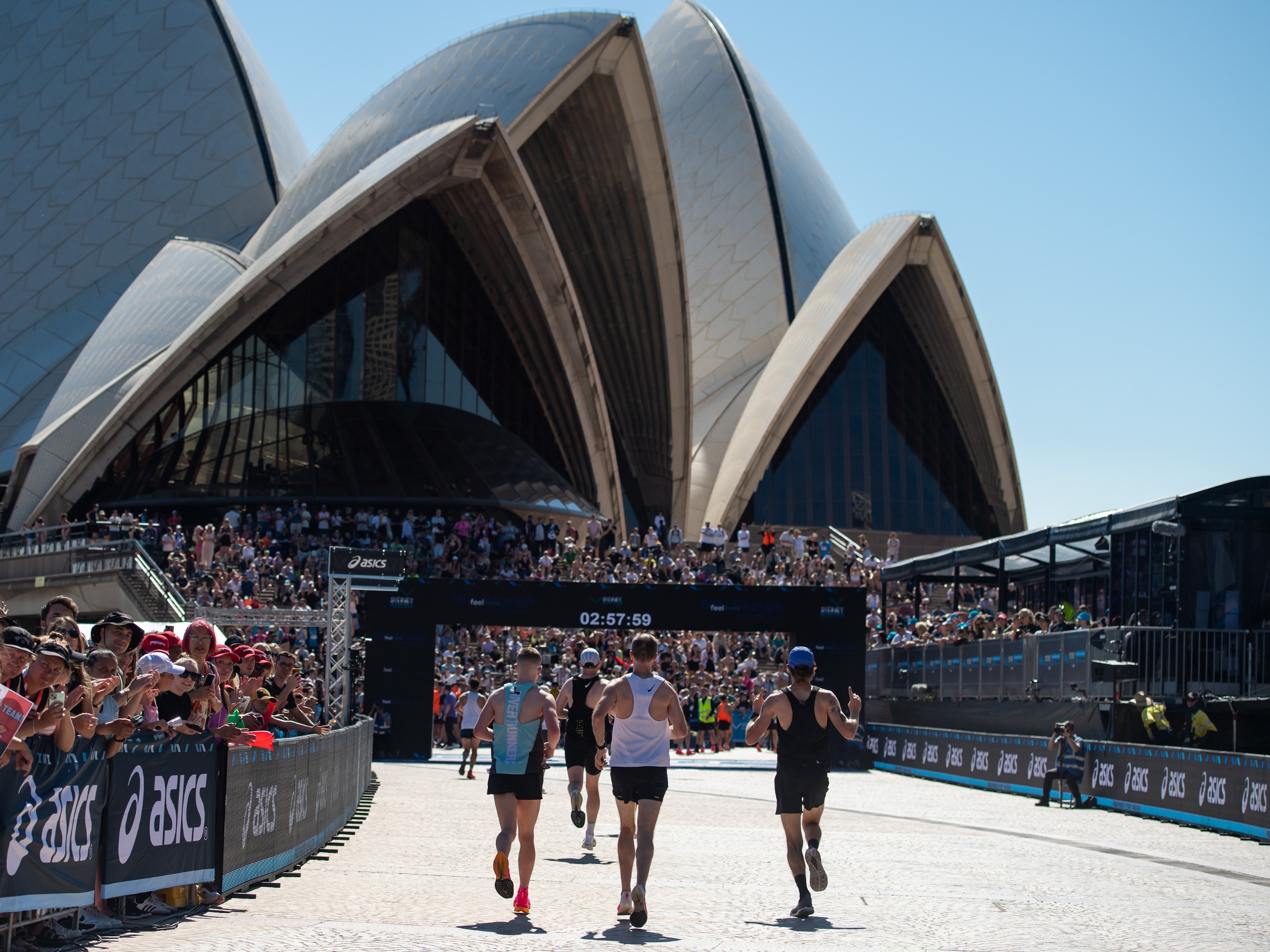 Coureurs arrivant devant l'Opéra de Sydney lors du TCS Sydney Marathon, entourés par une foule enthousiaste.