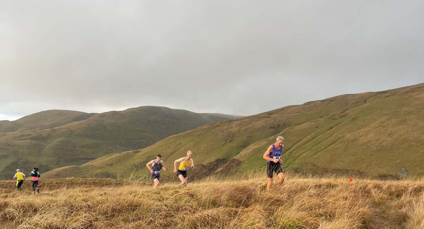 Groupe de coureurs traversant les hautes herbes dans les collines vallonnées des Ochil Hills.