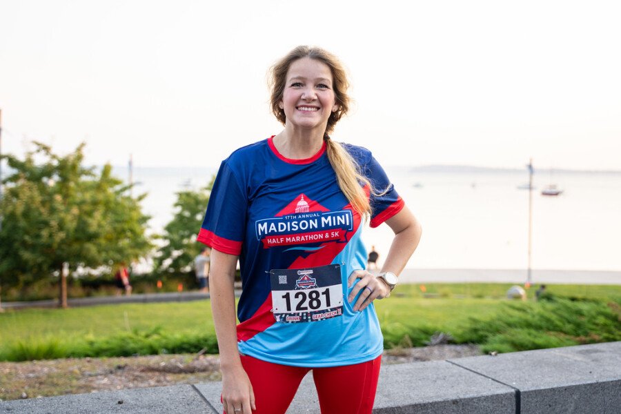 Une participante portant le maillot officiel du Madison Mini Marathon pose avec le lac Monona en arrière-plan.