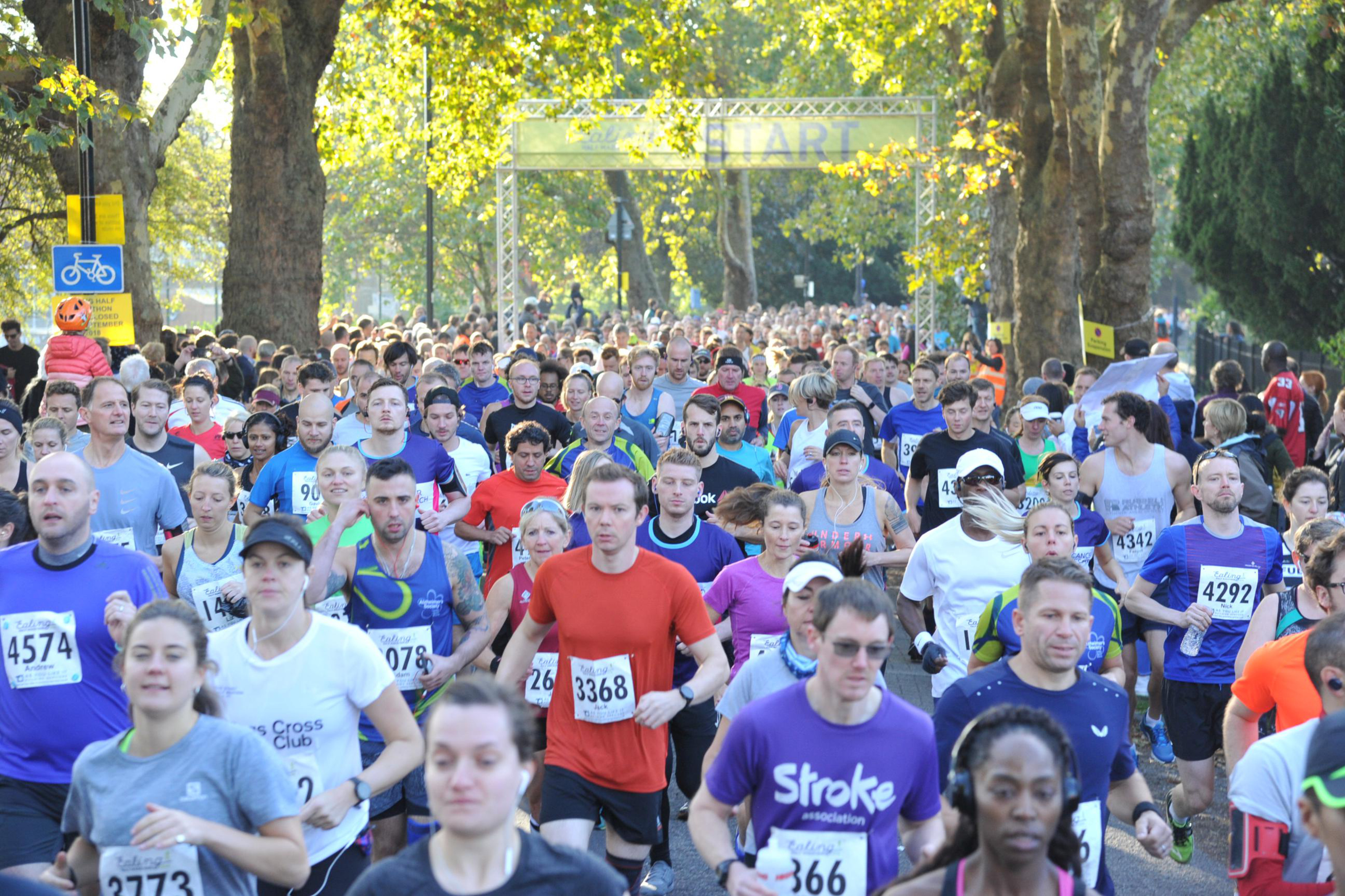 Départ de l'Ealing Half Marathon avec une foule dense de coureurs s'élançant sur le parcours dans un parc arboré de Londres.