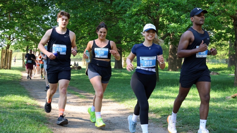 Groupe de coureurs souriants traversant Richmond Park lors de la course, sous les arbres verdoyants du parc.