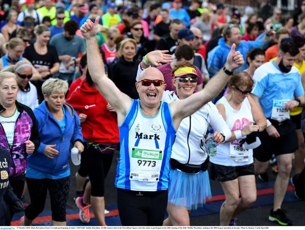 Coureur enthousiaste célébrant sa participation au marathon de Dublin avec les bras levés, entouré d'autres participants.