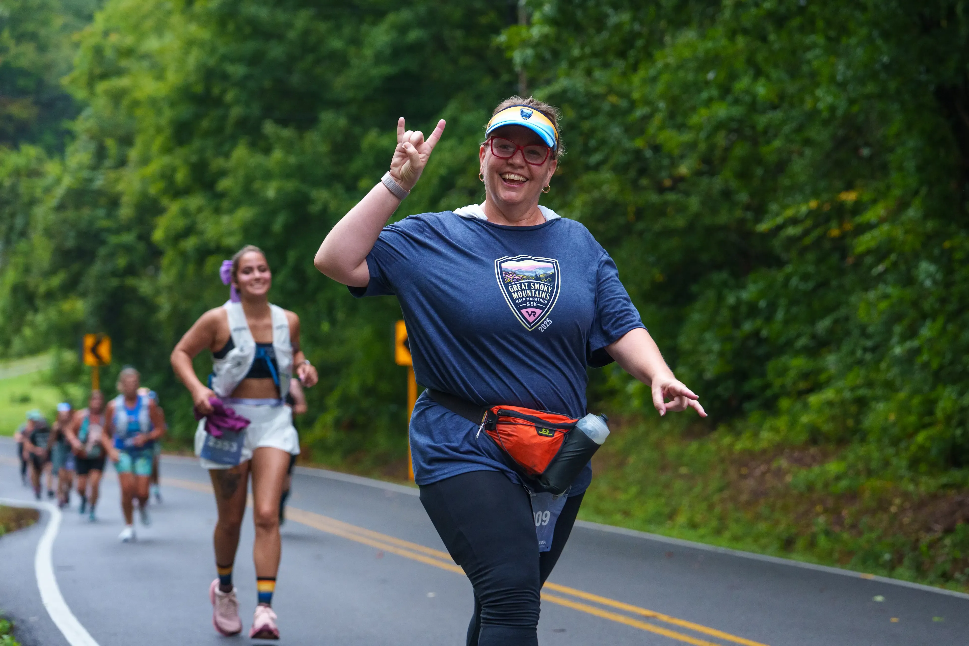 Coureuse souriante portant le t-shirt officiel Great Smoky Mountains sur le parcours vallonné entouré de forêts.