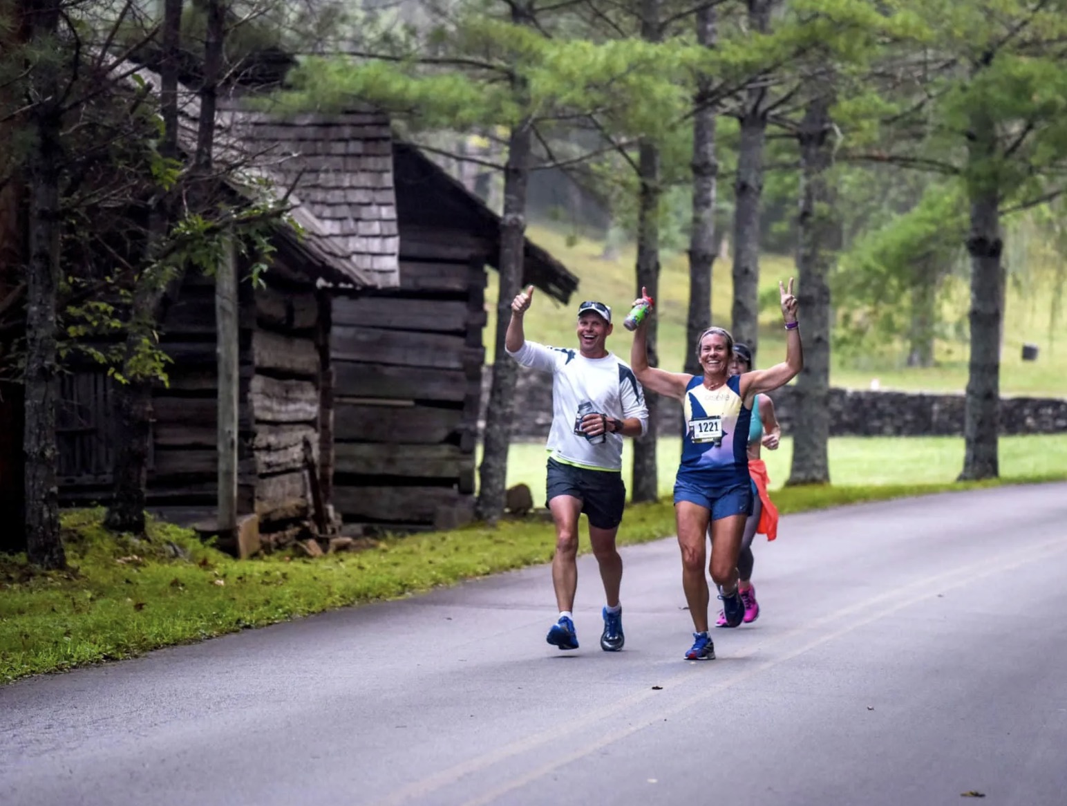 Deux coureurs joyeux célébrant leur course devant une cabane historique en bois typique du parc national.